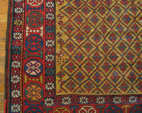 Low-pile geometric rug with a golden yellow diamond field and thick red, blue, and white border on wood flooring.