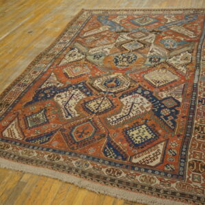 A rust and navy geometric tribal rug featuring complex diamond shapes lies on distressed wooden flooring.