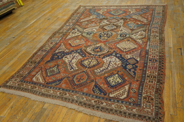 A rust and navy geometric tribal rug featuring complex diamond shapes lies on distressed wooden flooring.