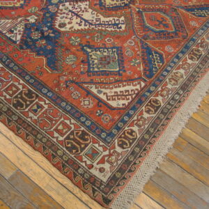 Red and dark blue geometric rug with multiple patterned borders and fringe rests on wood floorboards.