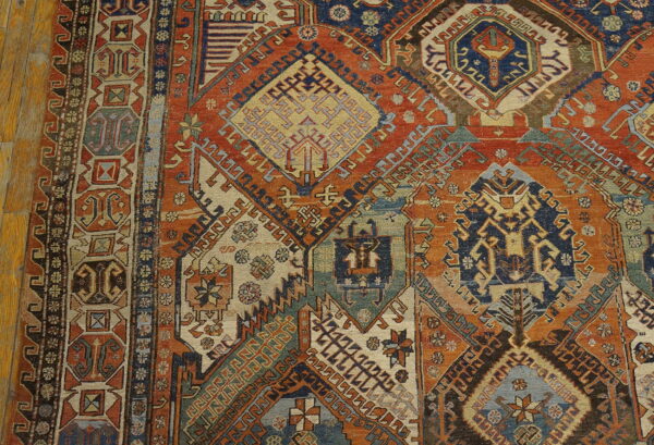 Intricate geometric diamond pattern rug in dominant rust orange, dark blue, and cream on wood planks.