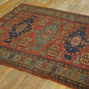 Low-pile rug featuring a red field, stylized blue and teal medallions, and geometric borders on wood flooring.