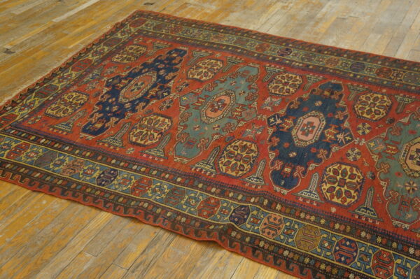 Low-pile rug featuring a red field, stylized blue and teal medallions, and geometric borders on wood flooring.