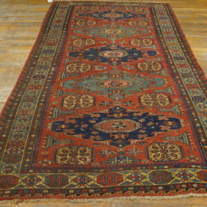 Geometric runner rug in deep red, navy, teal, and yellow on wide, distressed wooden floorboards.