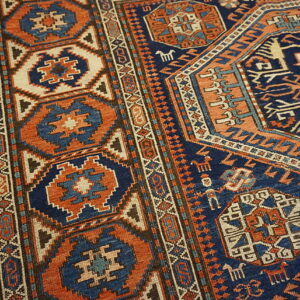 Geometric rug in navy and rust orange, showcasing complex borders and tribal motifs on light wood flooring.