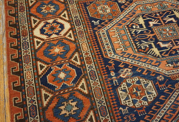Geometric rug in navy and rust orange, showcasing complex borders and tribal motifs on light wood flooring.