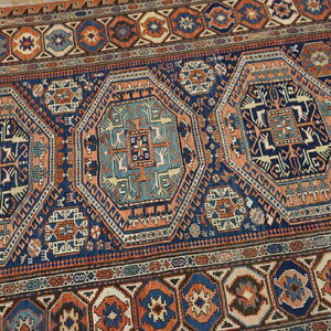 Geometric rug with navy, rust, and teal colors featuring linked octagonal medallions on light wood flooring.