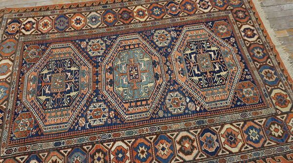 Geometric rug with navy, rust, and teal colors featuring linked octagonal medallions on light wood flooring.