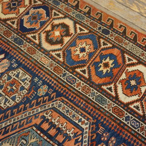 Geometric navy, terracotta, and cream rug detail lying diagonally on rustic light wood flooring.