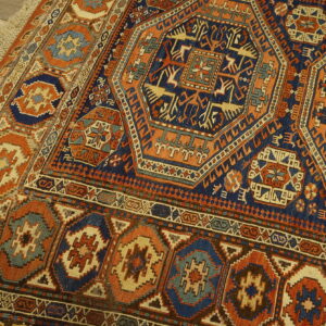 Geometric traditional rug in navy, burnt orange, and light blue with fringe lying on rustic wood floor.