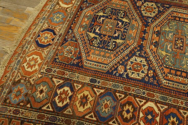 Geometric traditional rug in navy, burnt orange, and light blue with fringe lying on rustic wood floor.