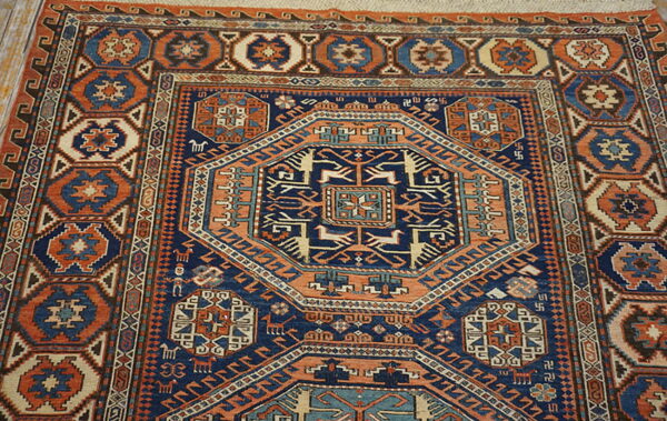 A densely patterned rug in navy, rust, and beige with a large geometric medallion rests on wood flooring.