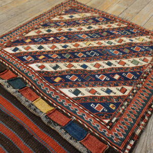 Geometric low-pile rug in blue, cream, and terracotta with patterned borders rests on rustic wood flooring.