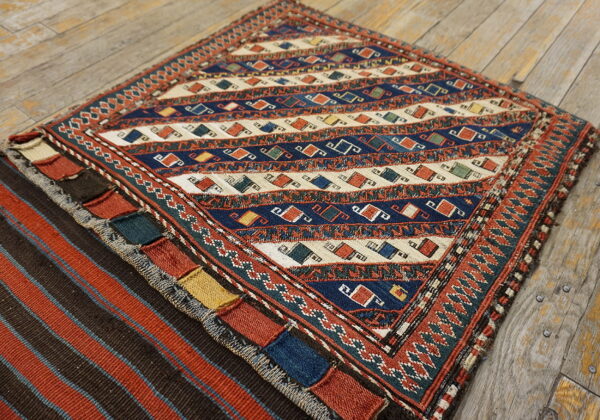 Geometric low-pile rug in blue, cream, and terracotta with patterned borders rests on rustic wood flooring.