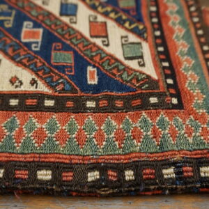 Geometric rug detail shows bands of woven patterns in indigo, rust, teal, and cream on a light wood surface.