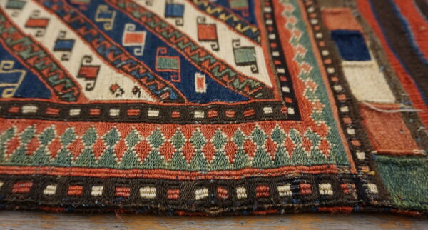 Geometric rug detail shows bands of woven patterns in indigo, rust, teal, and cream on a light wood surface.