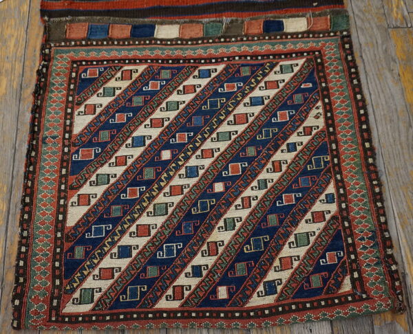 Geometric blue, cream, rust, and green flat-weave textile with diagonal stripes resting on wood flooring.