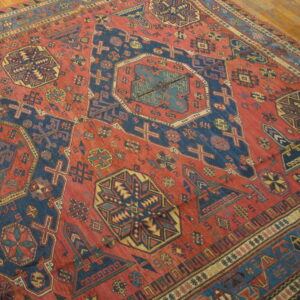 Geometric red rug with stepped navy and gold tribal motifs rests on light wood plank flooring.