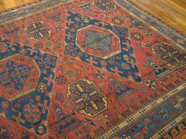 Geometric red rug with stepped navy and gold tribal motifs rests on light wood plank flooring.