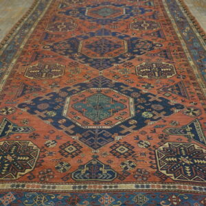 Large area rug featuring a terracotta field with repeating navy and cream geometric patterns on wood planks.