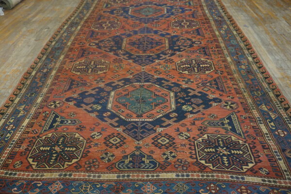 Large area rug featuring a terracotta field with repeating navy and cream geometric patterns on wood planks.