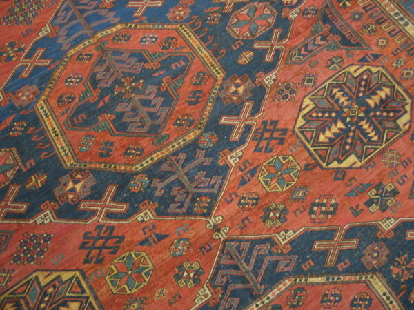 Traditional rug pattern featuring intersecting geometric motifs in red, dark blue, and gold.