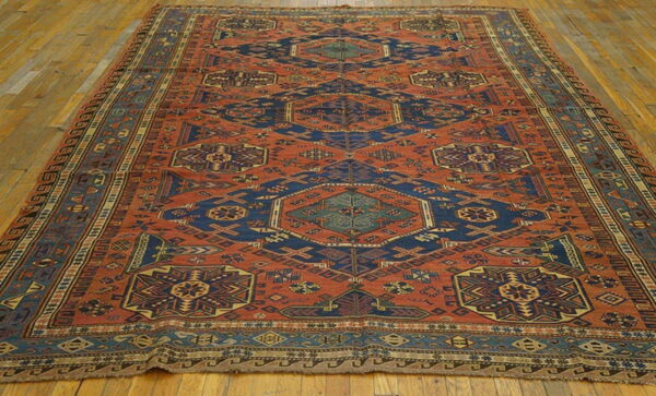A large geometric rug featuring rust, navy, and teal colors with central medallions on a wood plank floor.