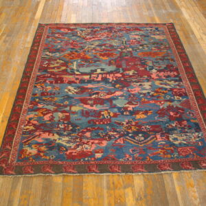 A rug with an abstract geometric pattern in blue, red, and pink rests on light rustic wood flooring.