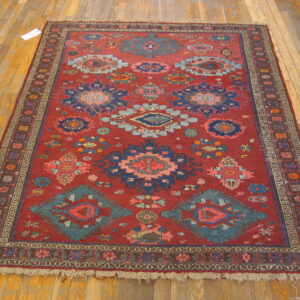 Red low-pile rug with geometric patterns in blue, teal, and pink rests on light plank wood flooring.