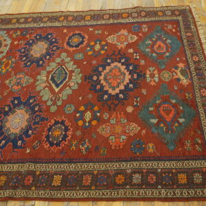 A low-pile red rug featuring multi-colored geometric medallions rests on distressed light wood flooring.