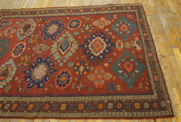 A low-pile red rug featuring multi-colored geometric medallions rests on distressed light wood flooring.
