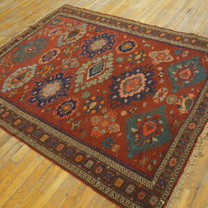 A rust red rug with geometric blue and green tribal motifs rests on light wood flooring.