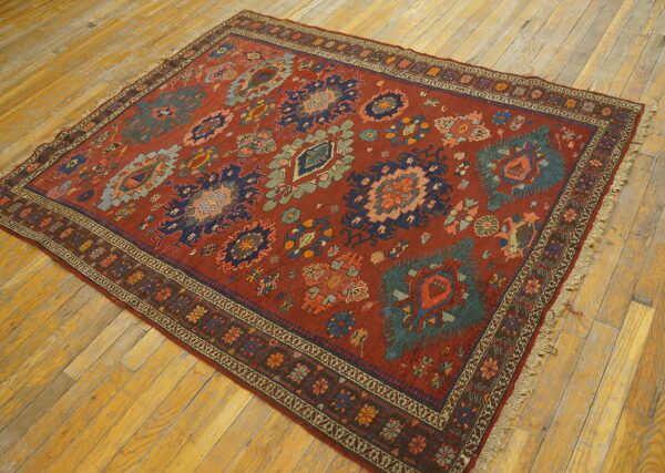A rust red rug with geometric blue and green tribal motifs rests on light wood flooring.
