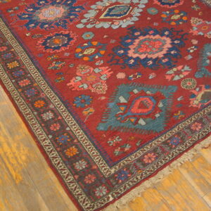 Close-up of a red geometric rug featuring teal and navy medallions on light brown hardwood floors.