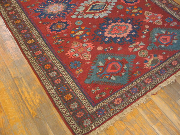 Close-up of a red geometric rug featuring teal and navy medallions on light brown hardwood floors.
