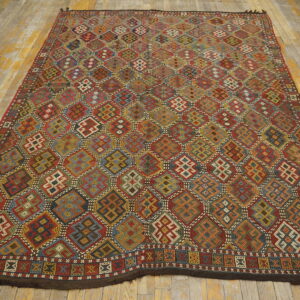 Multicolored flatwoven rug with repeating complex geometric patterns sits on worn yellow and grey hardwood flooring.