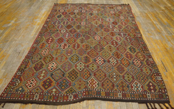 Multicolored flatwoven rug with repeating complex geometric patterns sits on worn yellow and grey hardwood flooring.