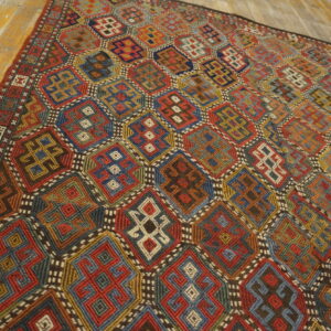 Vibrant geometric rug featuring complex octagonal patterns in red, blue, gold, and green on distressed wood.