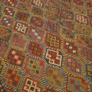 Low-pile rug with a complex geometric grid pattern in vibrant shades of red, blue, yellow, and green.