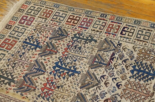 A flatweave rug displays intricate tribal patterns in blue, red, and beige on wooden planks.