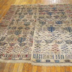 Beige rug featuring repeating tribal tree-like motifs and geometric borders lies on glossy hardwood floors.