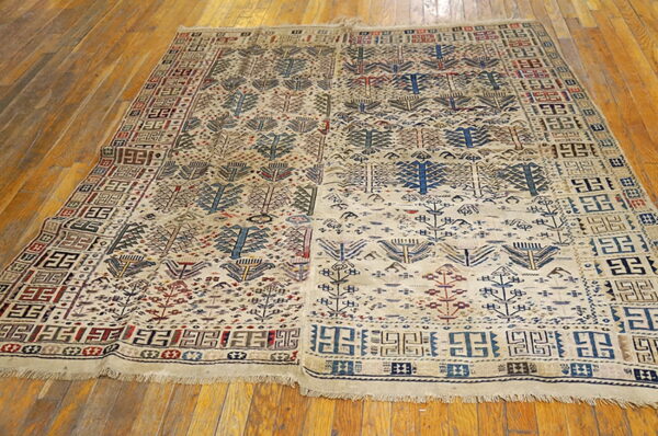 Beige rug featuring repeating tribal tree-like motifs and geometric borders lies on glossy hardwood floors.