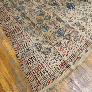 Beige rug with multicolored geometric motifs and stylized trees rests on worn wood flooring.