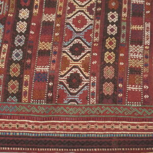 Flat-woven rug in deep red, patterned with complex geometric motifs and border bands in blue, green, and cream.
