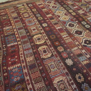 Flatweave textile displaying complex geometric patterns in vertical bands of deep red, gold, and blue.