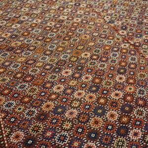 Low-pile rug featuring a complex geometric pattern in rust, navy, orange, and brown on a wood floor.