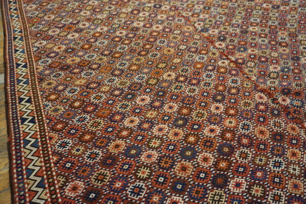 Low-pile rug featuring a complex geometric pattern in rust, navy, orange, and brown on a wood floor.