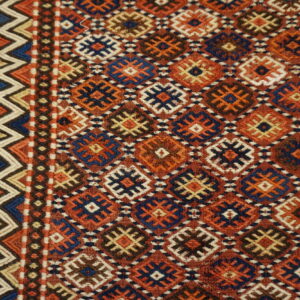 Terracotta flatwoven rug displaying repeating geometric diamonds, bordered by blue and cream zigzag stripes on wood floor.
