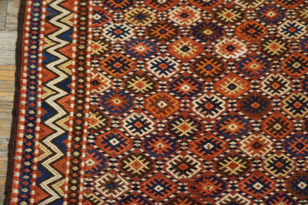 Terracotta flatwoven rug displaying repeating geometric diamonds, bordered by blue and cream zigzag stripes on wood floor.