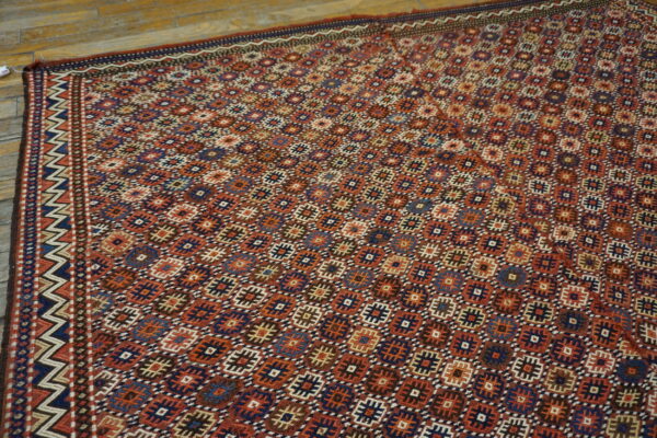 Rust and blue geometric flatweave rug with a chevron border lying on distressed wooden floors.